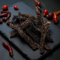 Dried beef jerky strips on a dark slate surface with red peppers.
