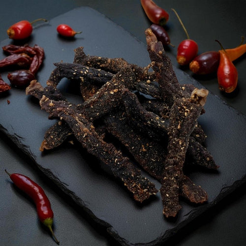 Dried beef jerky strips on a dark slate surface with red peppers.